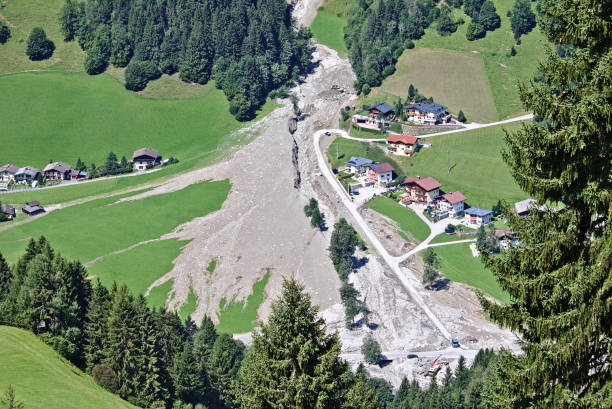Aerial view of mountain stream in the Austrian Alps blocked after a massive mudflow with excavator and truck working to clean up and small village nearby stock photo