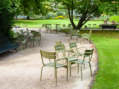 Typical metal lawn chairs of the public gardens of Paris scattered along an alley in the Luxembourg garden.