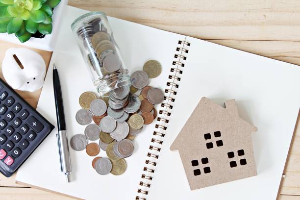 Flat lay or top view of wood house model and coins scattered from glass jar on open blank notebook paper Business, finance, savings, property ladder or mortgage loan concept : Flat lay or top view of wood house model and coins scattered from glass jar on open blank notebook paper cirrocumulus stock pictures, royalty-free photos & images