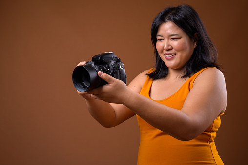 Studio shot of overweight Asian woman wearing yellow orange dress against colored background horizontal shot