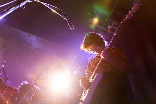 A young Japanese woman is playing the guitar during a live band event. Taken from a very low angle.
