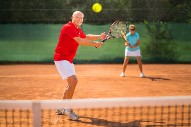 seniors taking on the world, smiling senior tennis player focusing ball on net - tennis active seniors healthy lifestyle senior men imagens e fotografias de stock