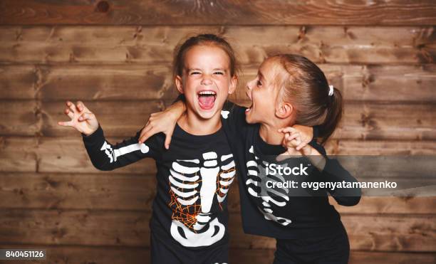 Holiday Halloween Funny Funny Sisters Twins Children In Carnival Costumes Skeleton On Wooden Stock Photo - Download Image Now