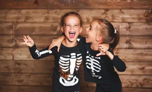 Photo of holiday halloween. funny funny sisters twins children in carnival costumes skeleton  on wooden