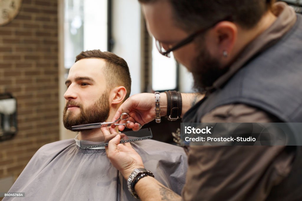 Barbe de style Barber avec des ciseaux au client au salon de coiffure - Photo de Barbier - Salon de coiffure libre de droits