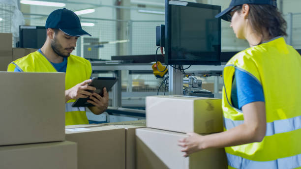 post sorting center worker puts cardboard boxes on belt conveyor while another worker using tablet pc. - post processing imagens e fotografias de stock