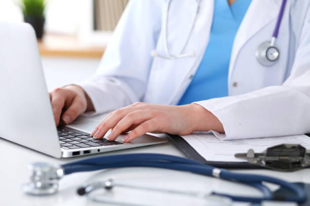 istock Close up of unknown female doctor typing on laptop computer while sitting  at the table 840458660
