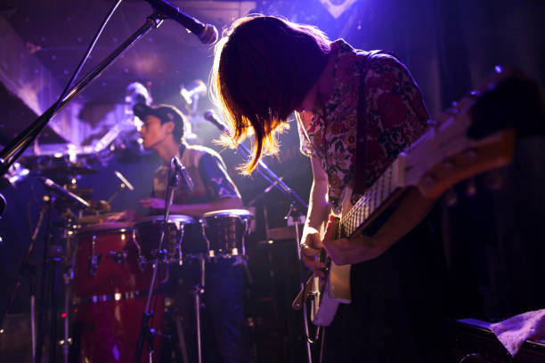 Woman Playing The Guitar A young Japanese woman is playing the guitar during a live band event. string ensemble stock pictures, royalty-free photos & images