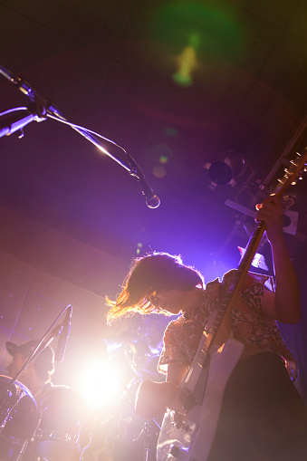 A young Japanese woman is playing the guitar during a live band event. Taken from a very low angle.