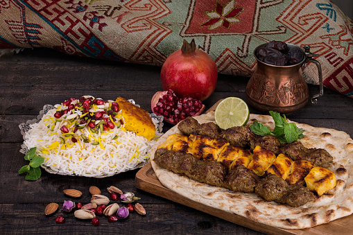 Tradicional del Medio Oriente persa cordero y pollo carne Kebab Shashlik (carne ensartada) parrilla sobre arroz azafrán y pan plano de pita y tahchin y granadas sobre un fondo oscuro. Cocina iraní photo