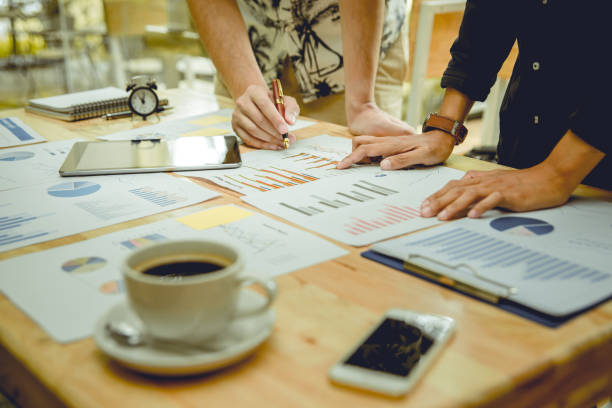 istock Two businessmen working and analyzing graphs papers on wooden table. there is cup of coffee and smartphone on table. Focus at businessmen. 840474430