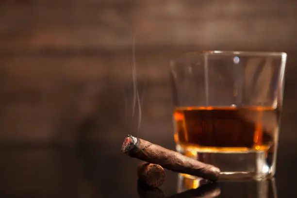 Photo of Smoking cigar and glass of whiskey in the background