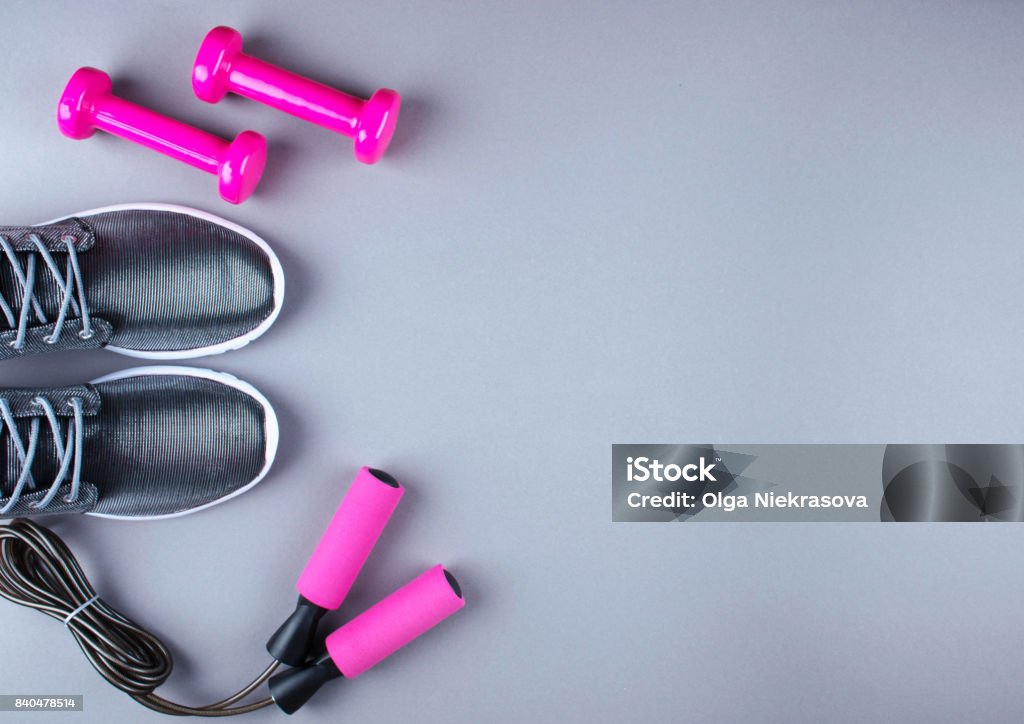 Flat lay shot of sneakers, jumpung rope and dumbbells. Flat lay shot of sneakers, jumpung rope and dumbbells on gray background with copy space for your text. Exercise Equipment Stock Photo