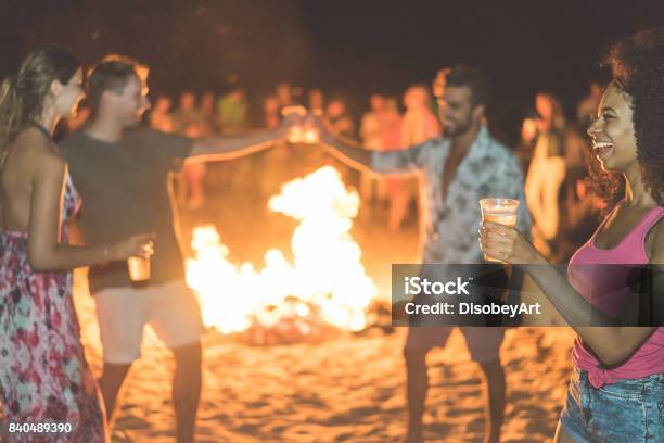 Foto de Férias Juventude Feriados E Festa Conceito Foco Suave No Vidro De Mão Garota Afro Quente Filtro De Verão Felizes Amigos Bebendo Cerveja No Festival De Praia Com Fogueira No Fundo Jovens Se Divertindo e mais fotos de stock de Festa