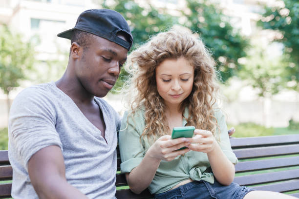istock Loving couple talking using smart-phone on bench in a park during summer 840489394