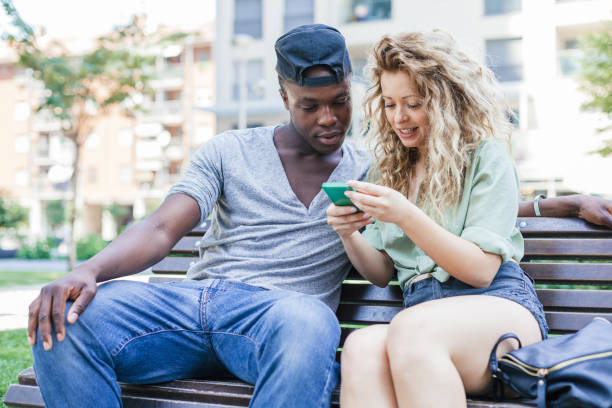 istock Loving couple talking using smart-phone on bench in a park during summer 840493010