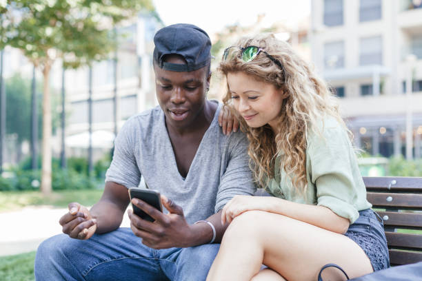 istock Loving couple talking using smart-phone on bench in a park during summer 840493182