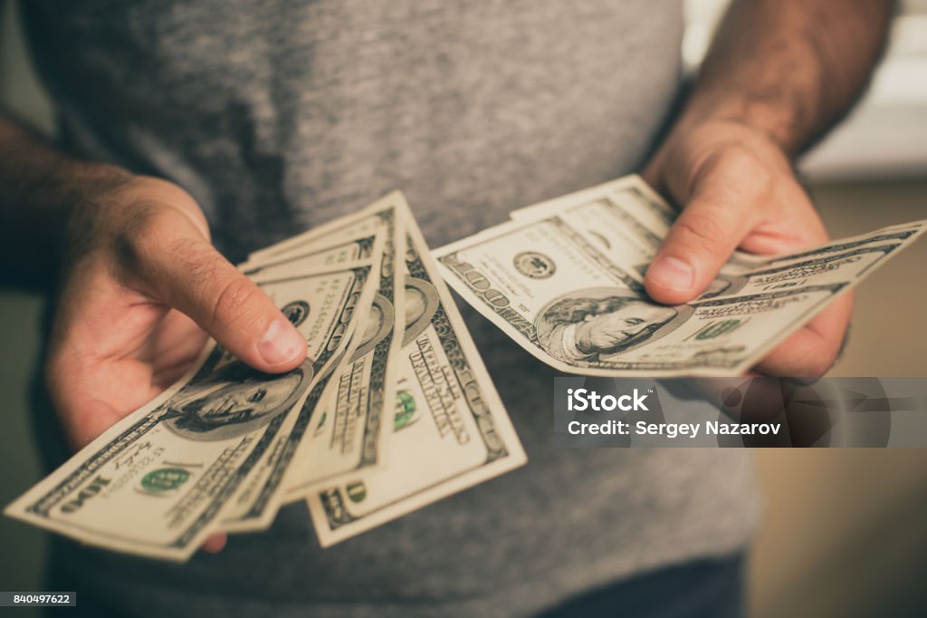 A man holds dollars in his hands A man in a gray T-shirt holds dollars in his hands. Bank. Casino. Salary. Rates. Currency Stock Photo
