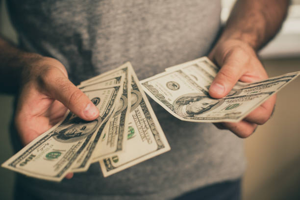 A man holds dollars in his hands A man in a gray T-shirt holds dollars in his hands. Bank. Casino. Salary. Rates. counting coins stock pictures, royalty-free photos & images