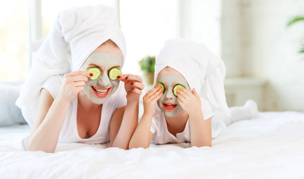 feliz madre de familia y niño hija hacen mascarilla piel - facial mask spa treatment cucumber human face fotografías e imágenes de stock