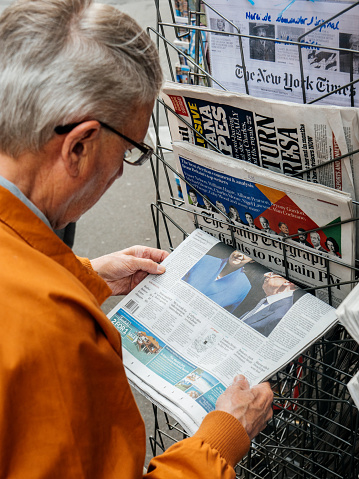 Paris: Senior man buying at press kiosk UK newspaper The Daily Telegraph with Theresa May picture and reactions to United Kingdom general election of 2017