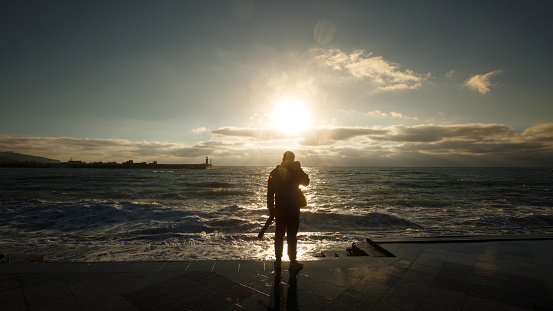 Silhouette of a man photographing the wave. Tourist photographer shoots stormy sea on wet embankment