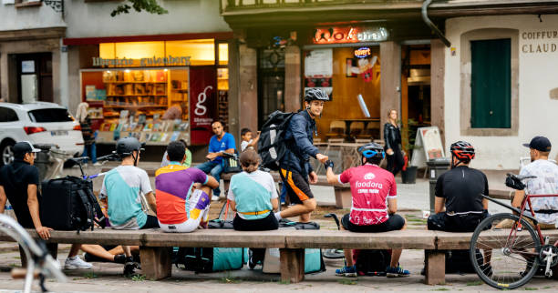 Deliveroo, Foodora and Uber Eats employees resting near their bikes Strasbourg: Deliveroo, Foodora and Uber Eats employees resting near their bikes eating lunch in city center ready to deliver on time the food to the client. meals on wheels photos stock pictures, royalty-free photos & images