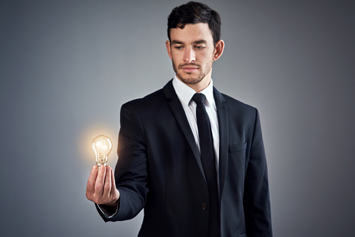 Studio shot of a young businessman holding a glowing lightbulb against a gray background