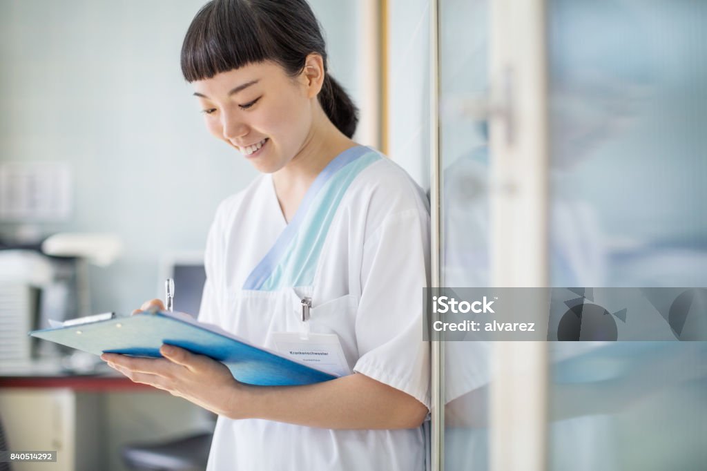 Nurse writing medical report at hospital Female medical professional working in clinic holding clipboard and writing patient history. Nurse writing medical report at hospital. Japanese Ethnicity Stock Photo