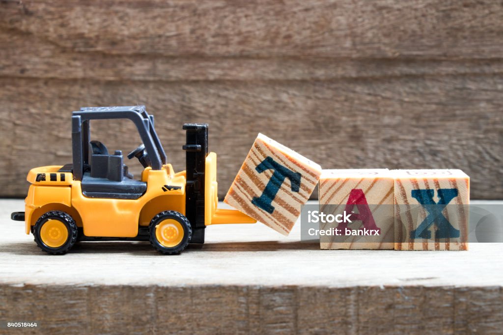 Toy plastic forklift hold block T to compose and fulfill wording TAX on wood background Tax Stock Photo