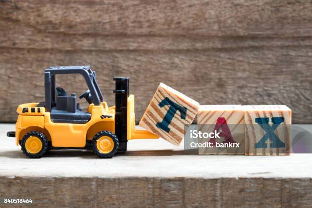 Toy Plastic Forklift Hold Block T To Compose And Fulfill Wording Tax On Wood Background Stock Photo - Download Image Now