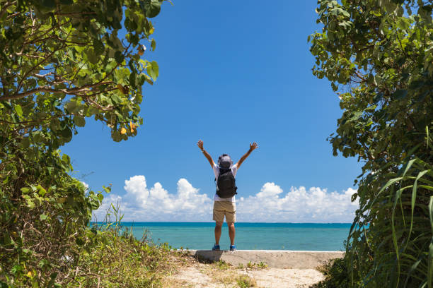 Young woman in a white dress jumping on the beach by the ocean. Happy vacation. Beach girl has fun by ocean. Excited girl jumping on white sand by beautiful blue sea.