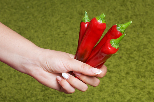 Red juicy hot pepper in a woman's hand. On a light green background.