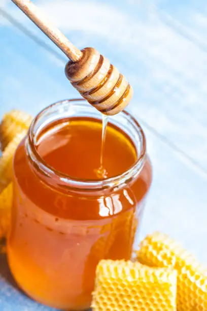 jar of honey with wooden honey dipper and honeycomb