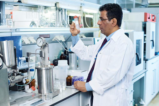 Serious mature Arabian scientist examining liquid in test tube after chemical reaction in laboratory