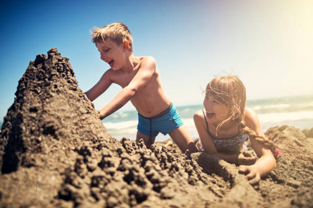 bruder und schwester eine sandburg am strand bauen - sandburg struktur stock-fotos und bilder