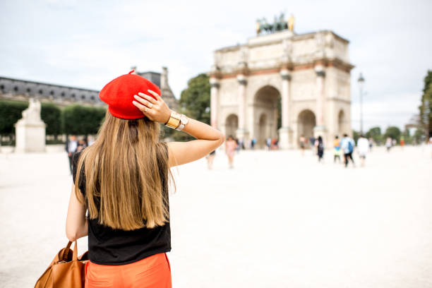 A beautiful female tourist in front of the Arc de Triomphe du Carrousel, situated at the entrance of Jardin de Tuileries, close to the beautiful buildings of the Louvre.