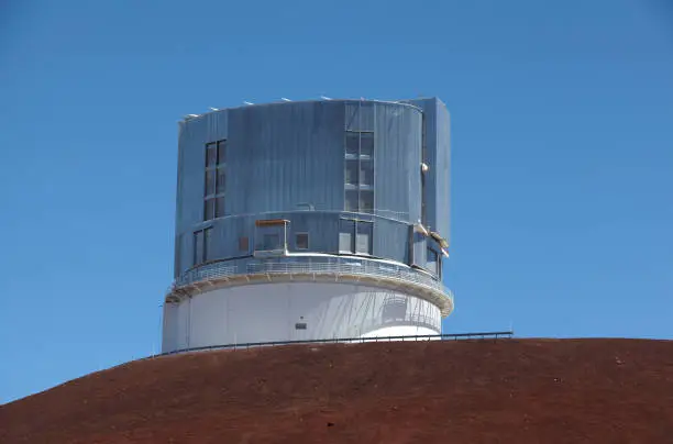 Telescop on mountain summit with volcanic landscape and blue sky