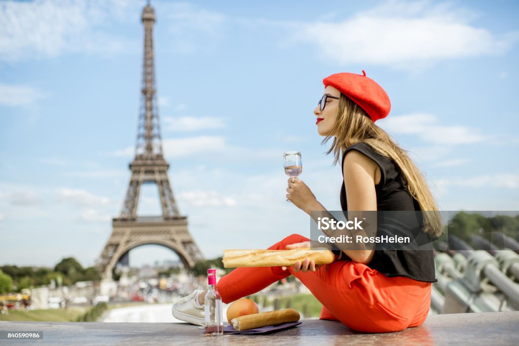 Woman having a picnic in Paris Young woman in red cap having a picnic with glass of wine and baguette sitting in front of the Eiffel tower in Paris France Stock Photo