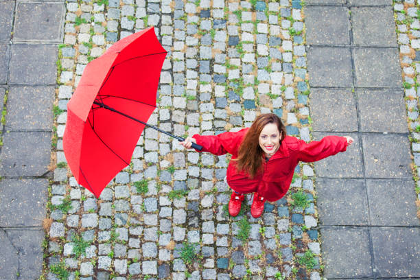 Young woman standing outdoors in the rain, holding red umbrella and looking at camera.