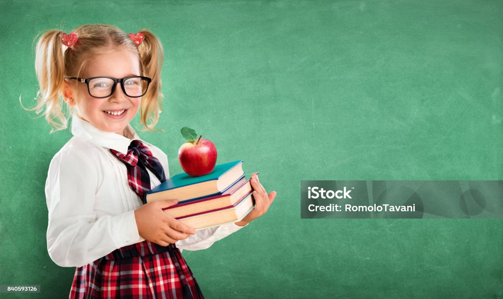 Little Schoolgirl Holding Books And Apple Student With Books And Apple And Blackboard On Background Back to School Stock Photo