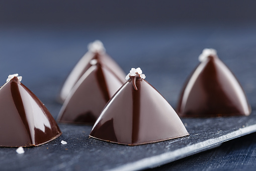 Luxury pyramid shaped chocolate candy on black background. Exclusive molded bonbons with salt decoration