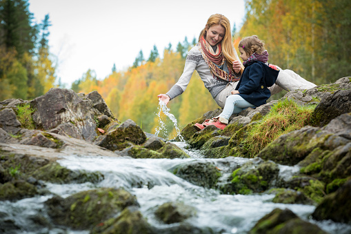 Sweet, cute little girl and mommy sitting on a rock in forest at stream. Enjoying fresh autumn air. Yellow trees. Karelia. Waterfall Kivach.
