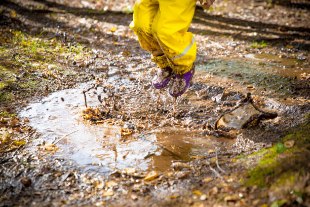 Cute little girl jumping in muddy puddle
