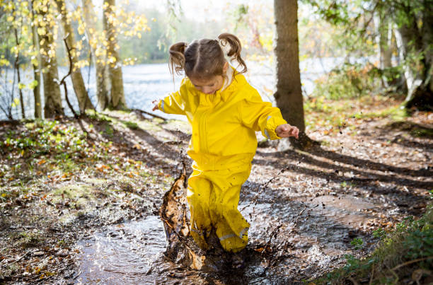 Cute little girl jumping in muddy puddle