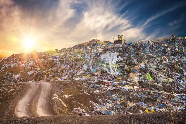 Photo of Pollution concept. Garbage pile in trash dump or landfill at sunset.