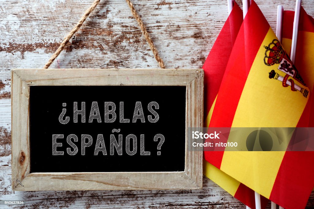 question hablas espanol? do you speak Spanish? a wooden-framed chalkboard with the question hablas espanol? do you speak Spanish? written in Spanish, and some flags of Spain against a rustic wooden background Spain Stock Photo