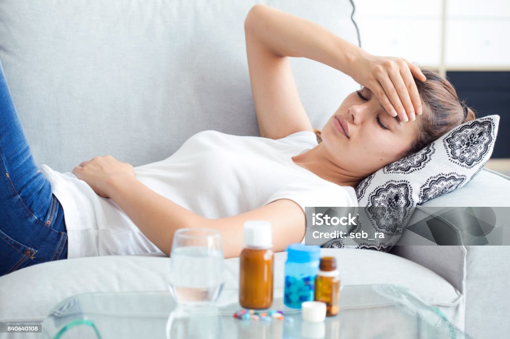 Sick young woman lying sofa Drinking Glass Stock Photo