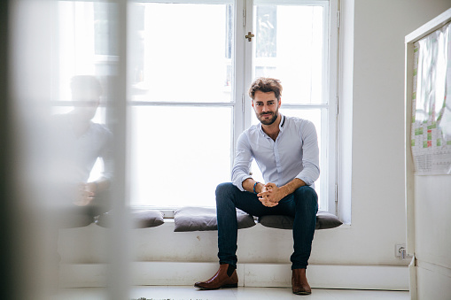 A portrait of a stylish office manager sitting by the window, looking at the camera.