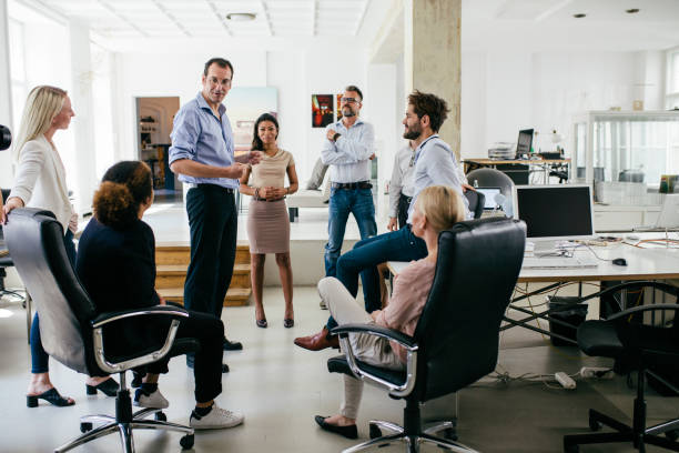 Local Office Manager Group Of Colleagues Holding Meeting In Modern Office Space A group of colleagues in a circle are holding a meeting together in a bright, modern office space. local office manager stock pictures, royalty-free photos & images